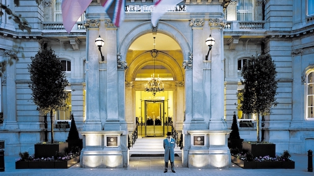 Doorman stands in front of the ornate entrance of the Langham Hotel in London.