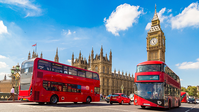 Two red London buses pass in front of Big Ben and the Houses of Parliament on a sunny day.