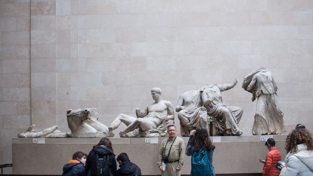 Tourists stand next a large grey statue at the british museum.