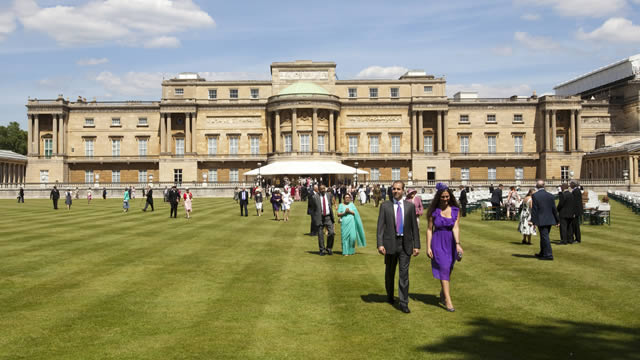 Des visiteurs marchent sur la pelouse des jardins de Buckingham Palace.