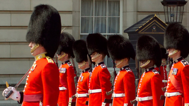 The formal Changing of the Guard ceremony at Buckingham Palace, with the guards dressed in traditional red tunics and bearskin hats