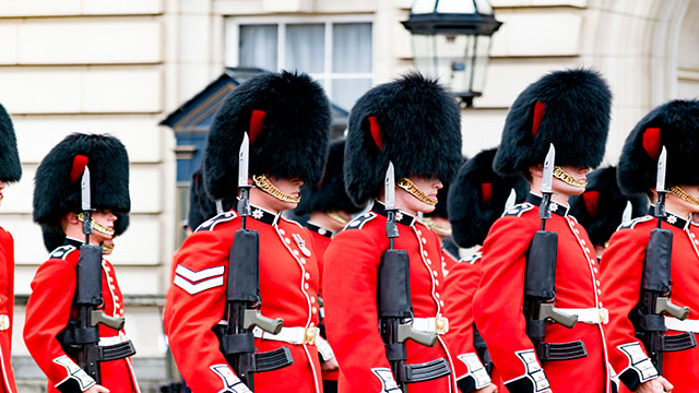 Un groupe de soldats du palais de Buckingham est vu paradant dans la cour, tous portant l'uniforme traditionnel et les chapeaux en peau d'ours. 