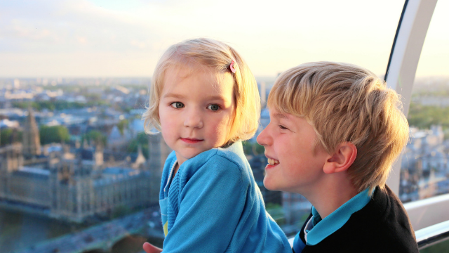 Two young children looking out at of the London Eye with the Houses of Parliament in the backdrop. 