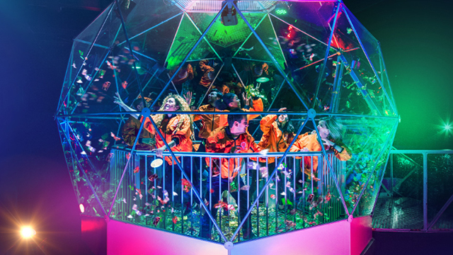 A group of gamers, wearing orange, try to catch falling items within the colourfully lit dome, as part of the Crystal Maze LIVE Experience.