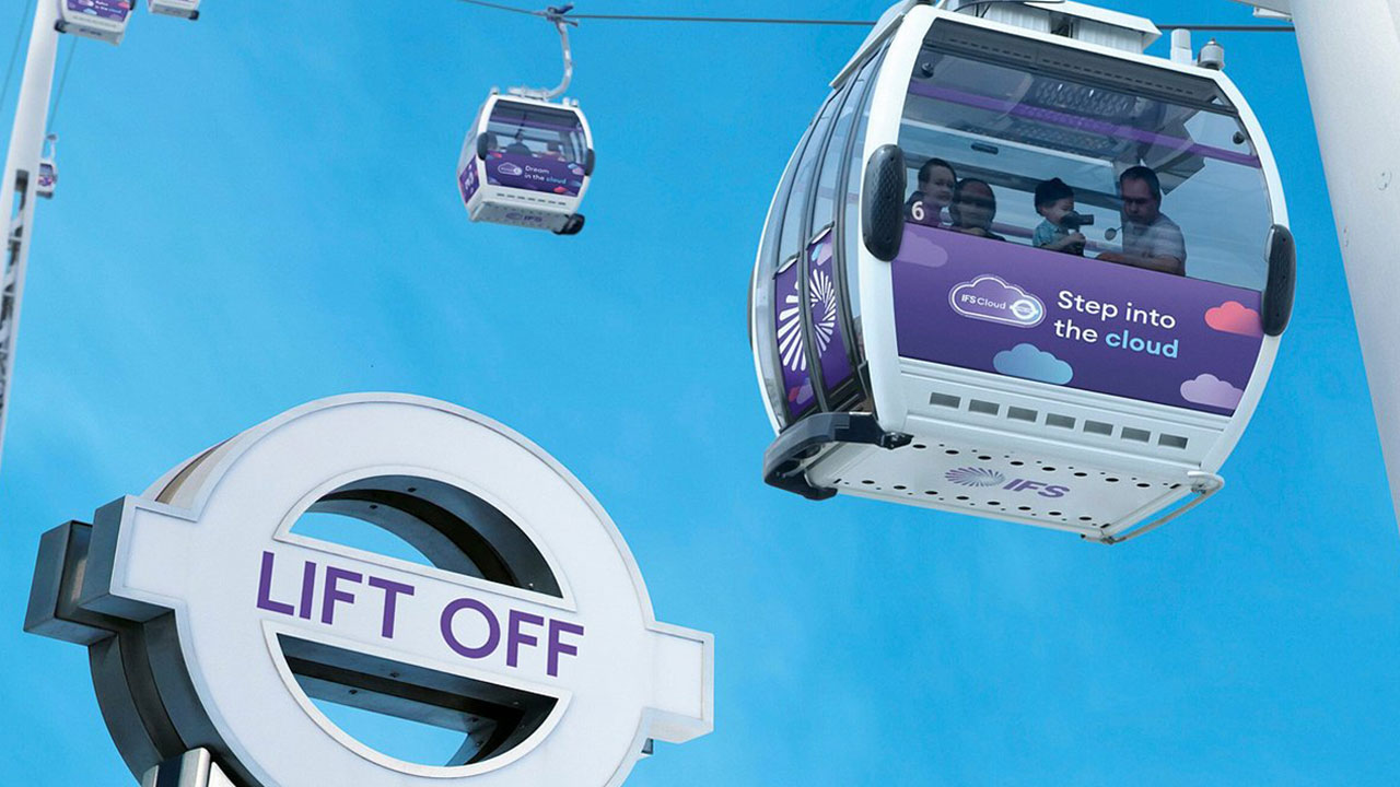 Die lilafarbenen IFS Cloud Cable Cars fliegen über ein Schild von Transport for London mit der Aufschrift Lift Off.