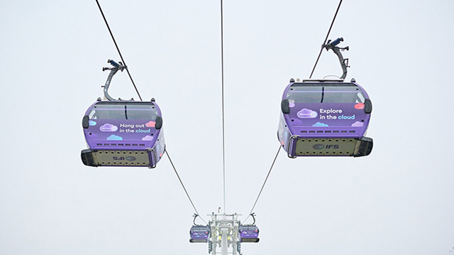 Two purple cable cars are flying over the river in London going in both directions.