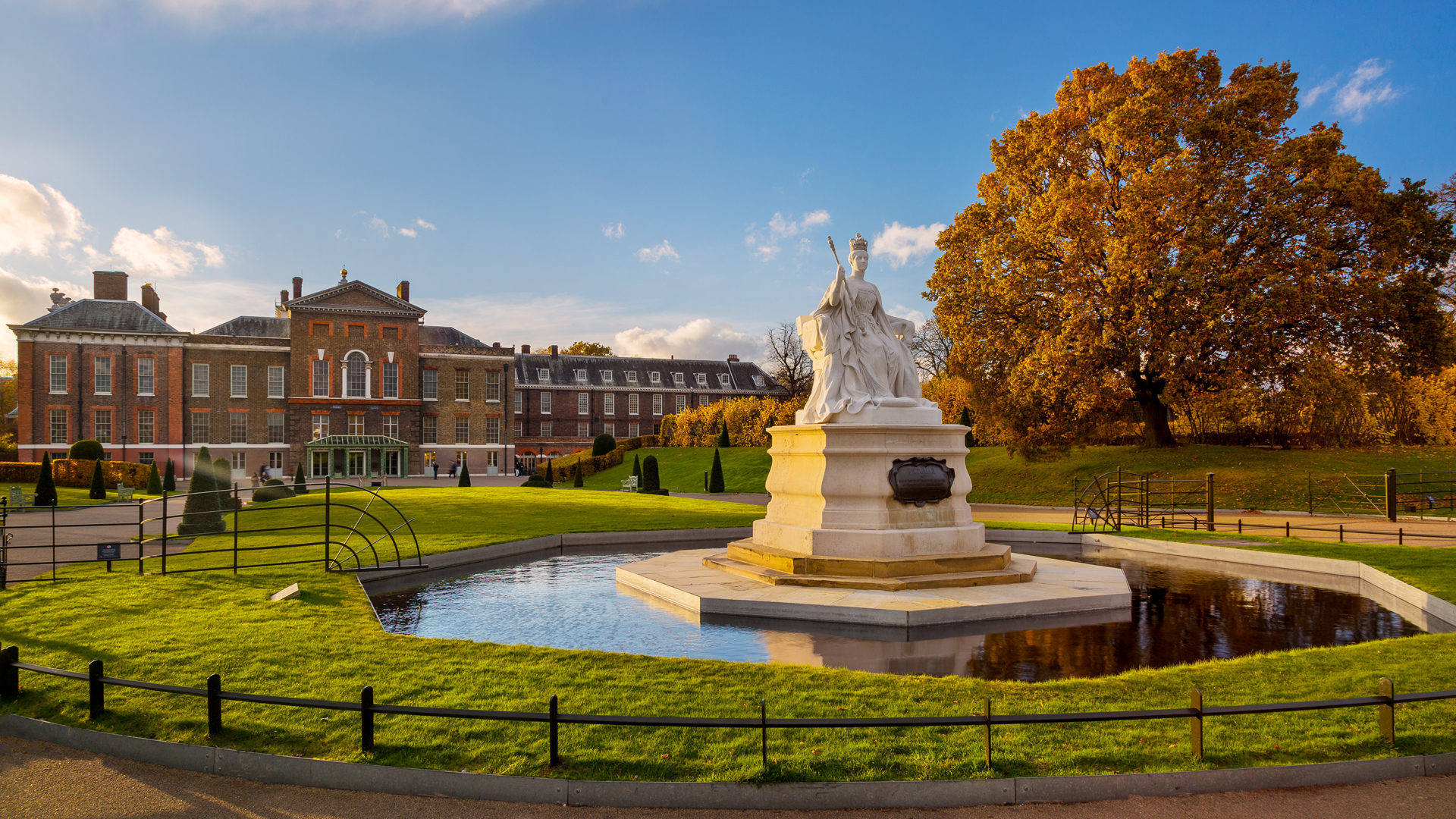 Queen Victoria statue in Kensington Gardens, with tree with autumn leaves, and Kensington Palace in the background
