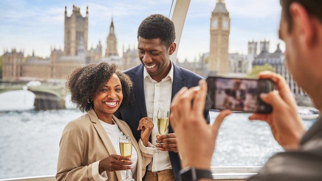 A couple pose of photo with a glass of sparkling wine in hand while on the London Eye, with the Houses of Parliament and Big Ben in the background.