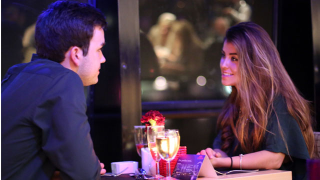 Two people sit at a table cheersing glasses.