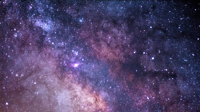 A galaxy of stars in the night sky with hues of violet, purple and pink.