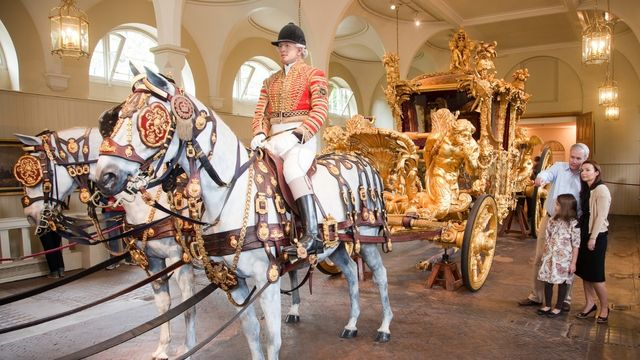A family look at the bright golden state coach being pulled by horse and human figures at the royal mews nearby buckingham palace. 