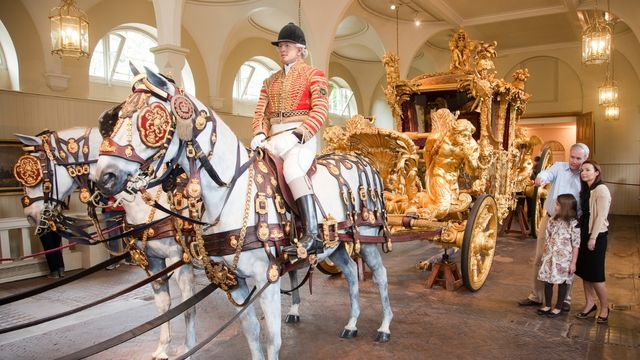 A family look at the bright golden state coach being pulled by horse and human figures at the royal mews nearby buckingham palace.