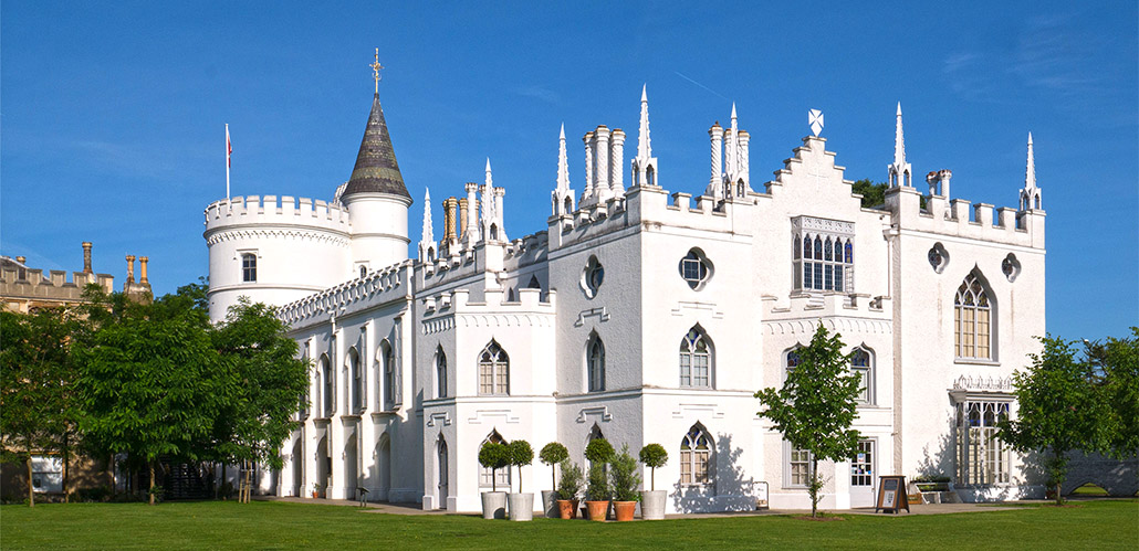 Strawberry Hill House, a white turreted castle, sits upon a grassy hill in front of a blue sky. 