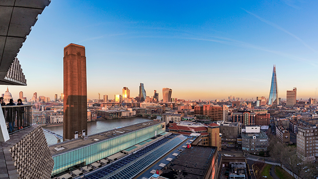 Looking out at Tate Modern's Turbine Hall tower, and the London skyline, with the Shard and City of London skyscrapers on the horizon, at dusk.