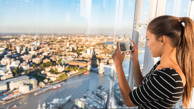 Young woman smiling while she takes a picture of the view of London and the river Thames from The View from The Shard.