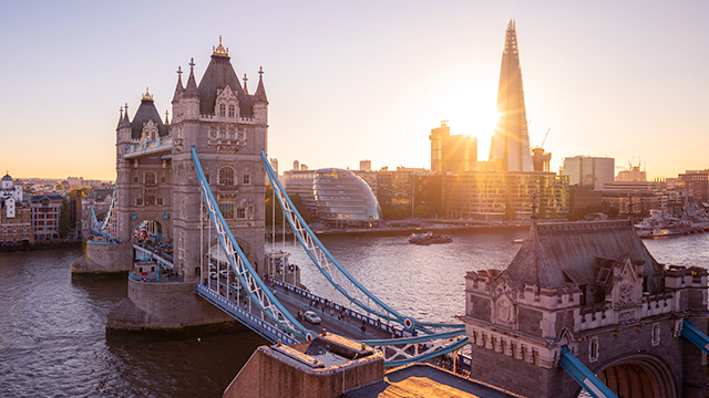 A panoramic view of Tower Bridge and the Thames at sunset, with City Hall and The Shard in the background.