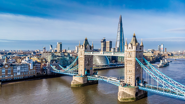 An aerial view of Tower Bridge on a bright day, with The Shard and City Hall in the background.