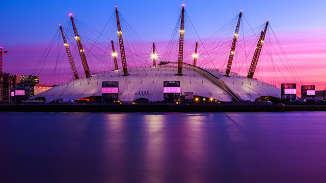 The O2 arena lit up at sunset against purple and pink sky.