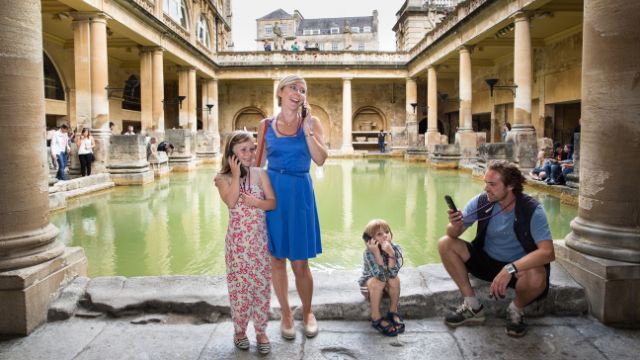 A family enjoy a tour of the Roman Baths in Bath on a day trip from London.