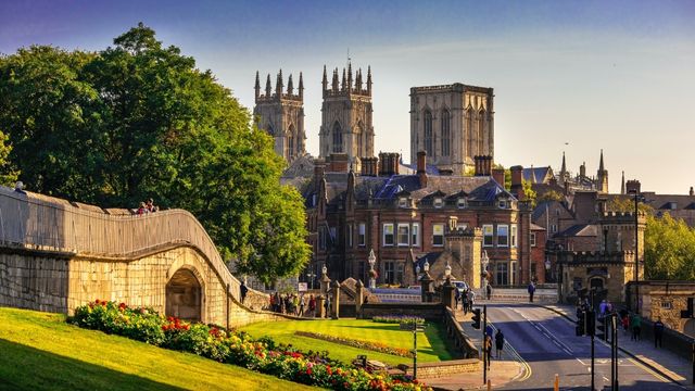 A bright blue sky above historic buildings in York including a majestic cathedral and people walking along a medieval wall.