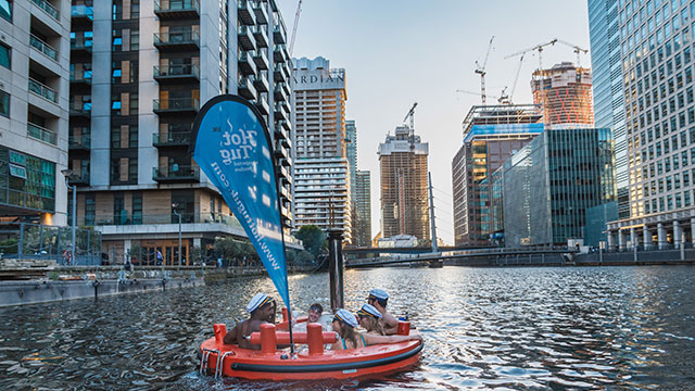 A group of five people male and female wearing sailors hats cruising along the Thames in a Skuna Hot Tub Boat