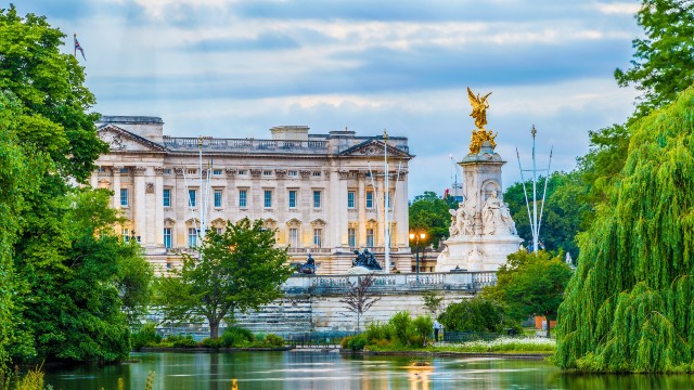 Buckingham Palace and the Victoria Memorial at dusk, with pond and water features and trees in the foreground.
