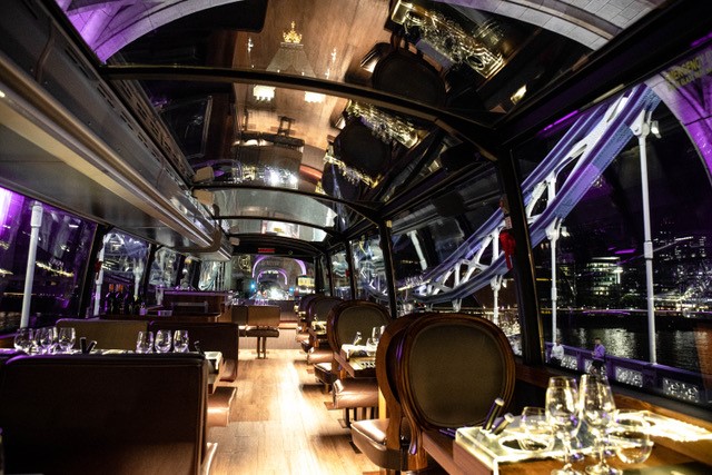 A food tour bus with booths and tables covered in plates, glasses and cutlery under a glass ceiling.