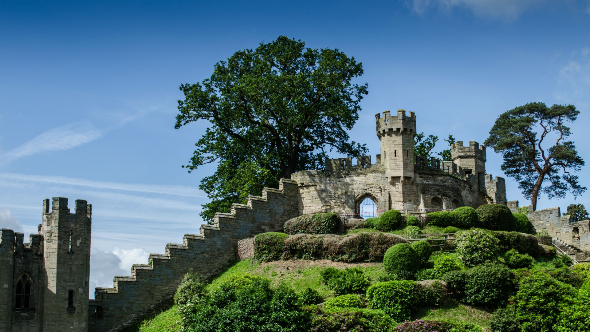 Photo of Warwich castle amongst green trees with blue sky in the background.
