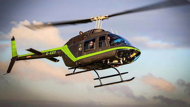 Un hélicoptère noir et vert en vol avec des passagers à bord.