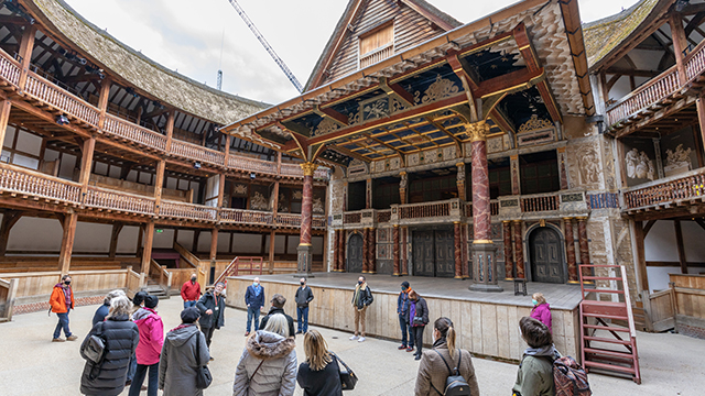 A small group of people, wearing face coverings, gather in front of the stage at Shakespeare's Globe Theatre.