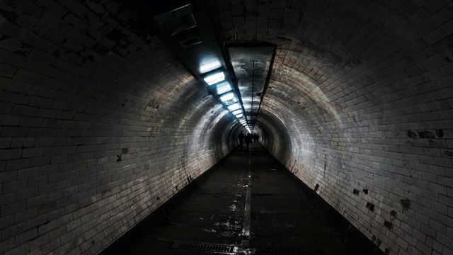 A group of people walk through the dimly lit greenwich tunnel at night.