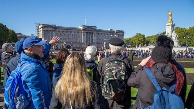 A group of tourists stand in front of Buckingham Palace in London with their tour guide on the Royal Walking Tour, Changing of the Guard. 