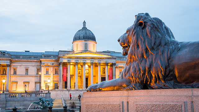 A Trafalgar Square lion at dusk in front of the National Gallery