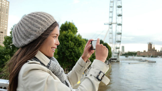 Woman taking a picture with the London Eye skyline.