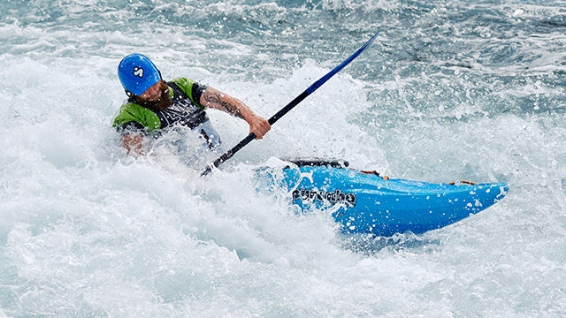 A man in a cblue anoe turns in the rapids of the Lee Valley White Water Centre.