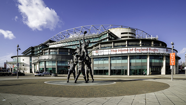 The exterior of Twickenham Stadium, with a statue of rugby players catching a ball at a lineout. Taken on a clear day.