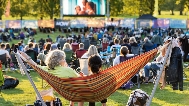 Two people sitting on a hammock behind a group watching a film outdoors in London.