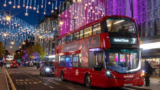 Der legendäre rote Doppeldeckerbus in London bei Nacht mit Weihnachtsbeleuchtung im Hintergrund