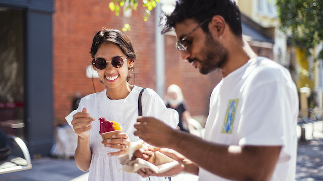 A woman and a man eat ice cream on a street in London on a sunny day