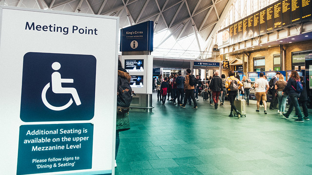 Sign at a London airport that says, 'Meeting point' and has a symbol of a person in a wheelchair