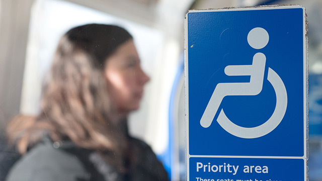 Woman sitting on the London Underground behind a sign with a wheelchair symbol that says "Priority area"