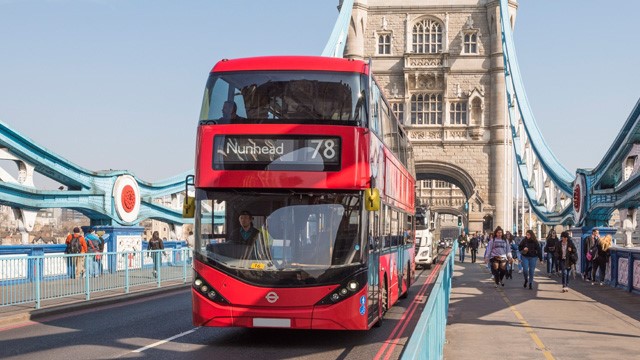 A red London bus driving across Tower Bridge on a sunny day