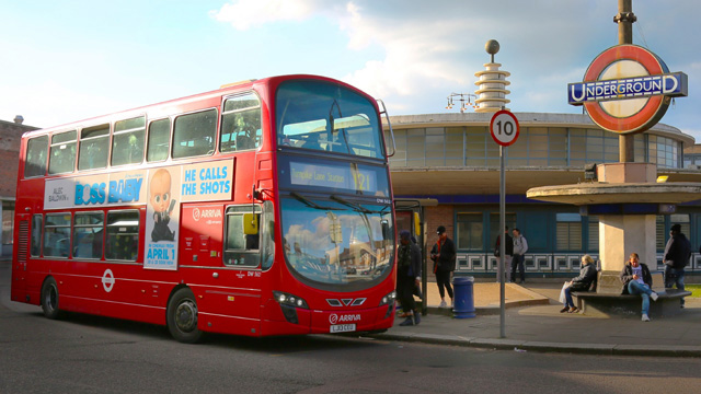 A red London bus waiting at the bus stop as people queue near a London Underground station.