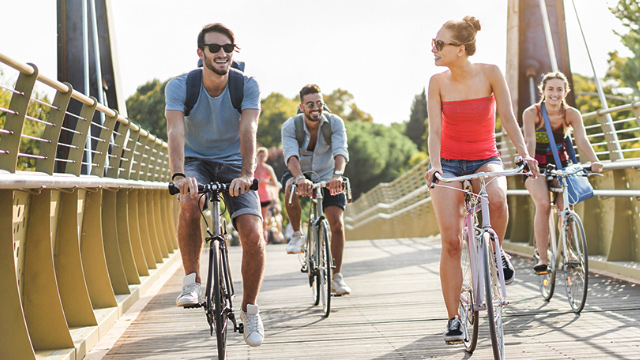 A group of four young people cycling on a bridge in London on a summer's day.