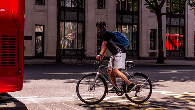 A man cycling behind a red London bus.