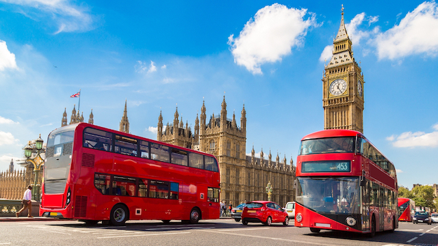 Two red buses and a red car in front of the Houses of Parliament and Big Ben in London on a sunny day