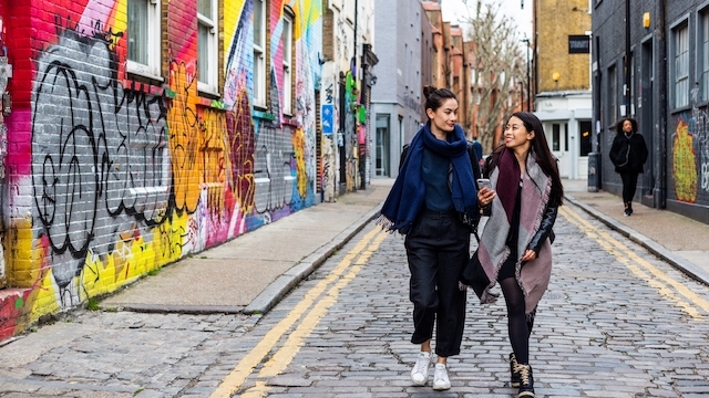 Two women walk down a narrow road past colourful street art in Shoreditch, East London.
