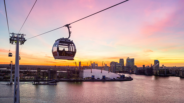 One of the IFS Cloud Cable Cars rises high above the Thames at sunset, with The O2 in the background.