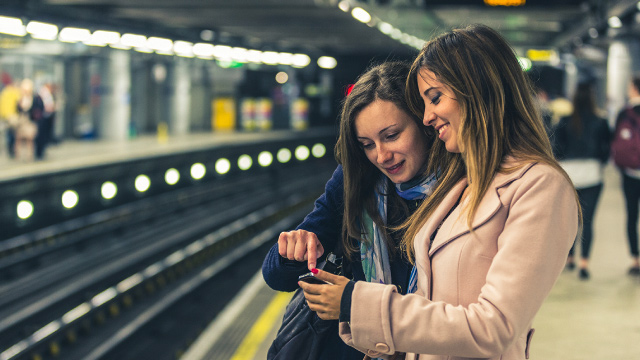 Two women look at a smartphone on a Tube platform on the London Underground.