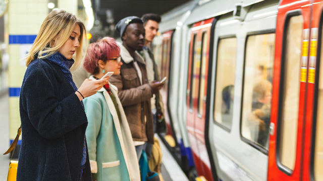 Woman looking at her phone on a London Underground platform with a Tube train in the background
